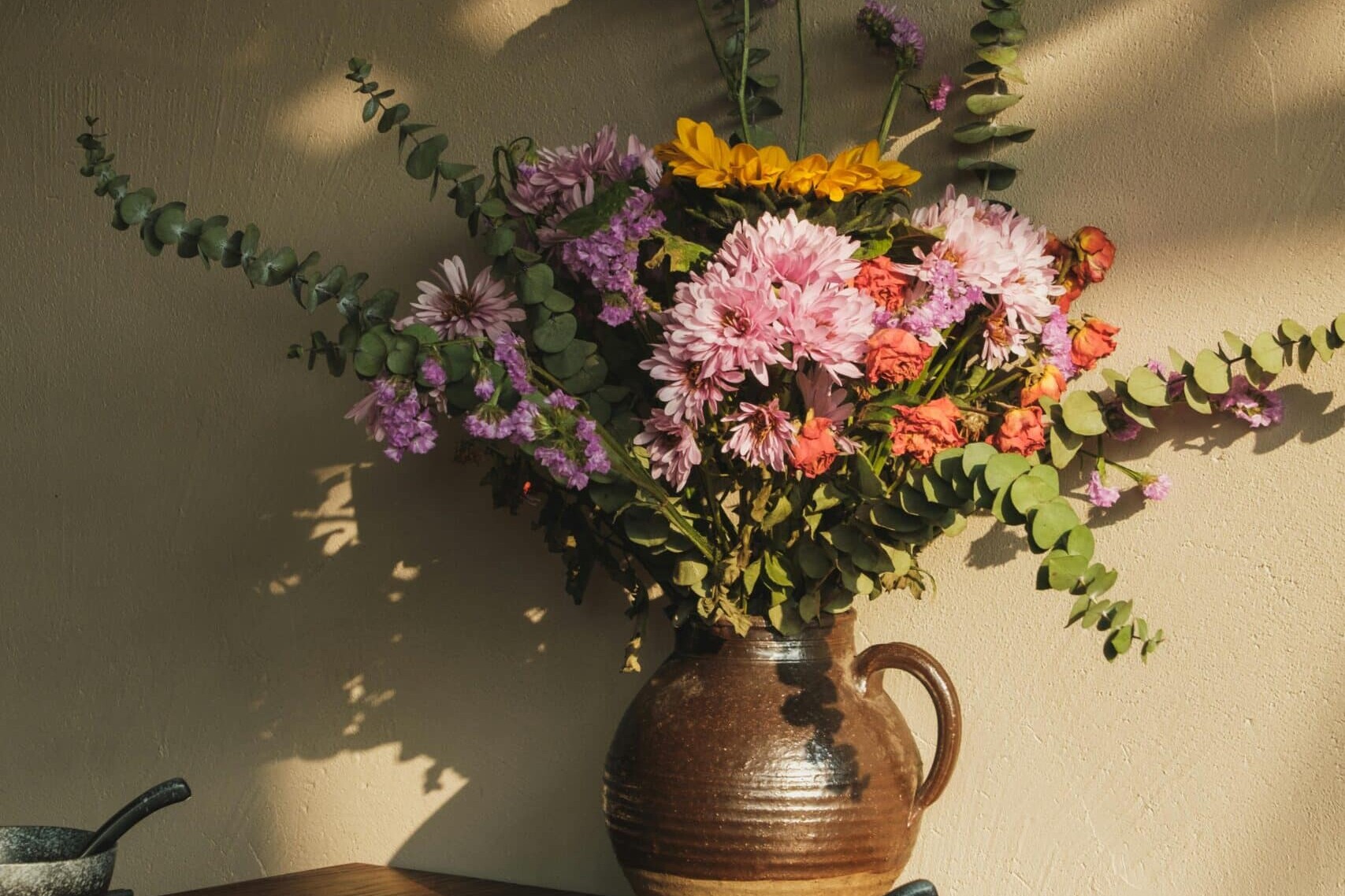 Keramiek servies en vaas op een houten eettafel met een grote bos lentebloemen.